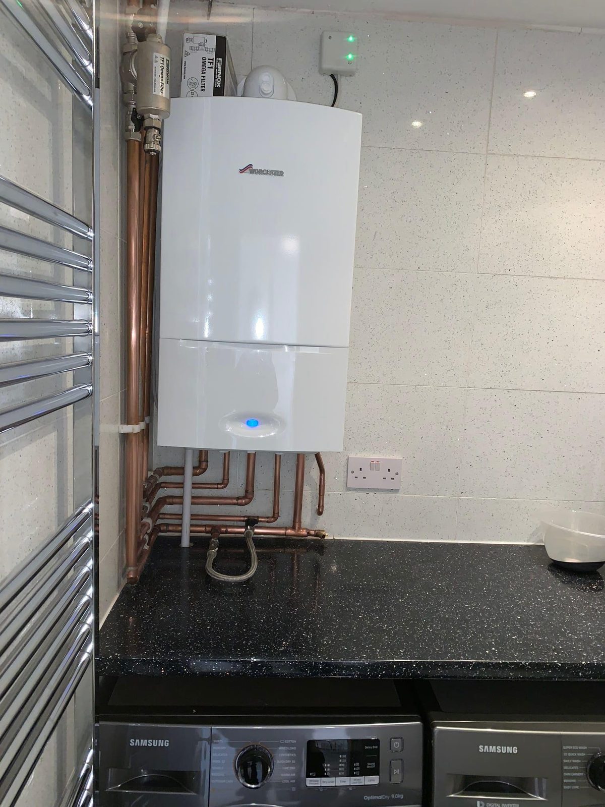 White boiler on a tiled wall above a dark worktop, next to a towel rail