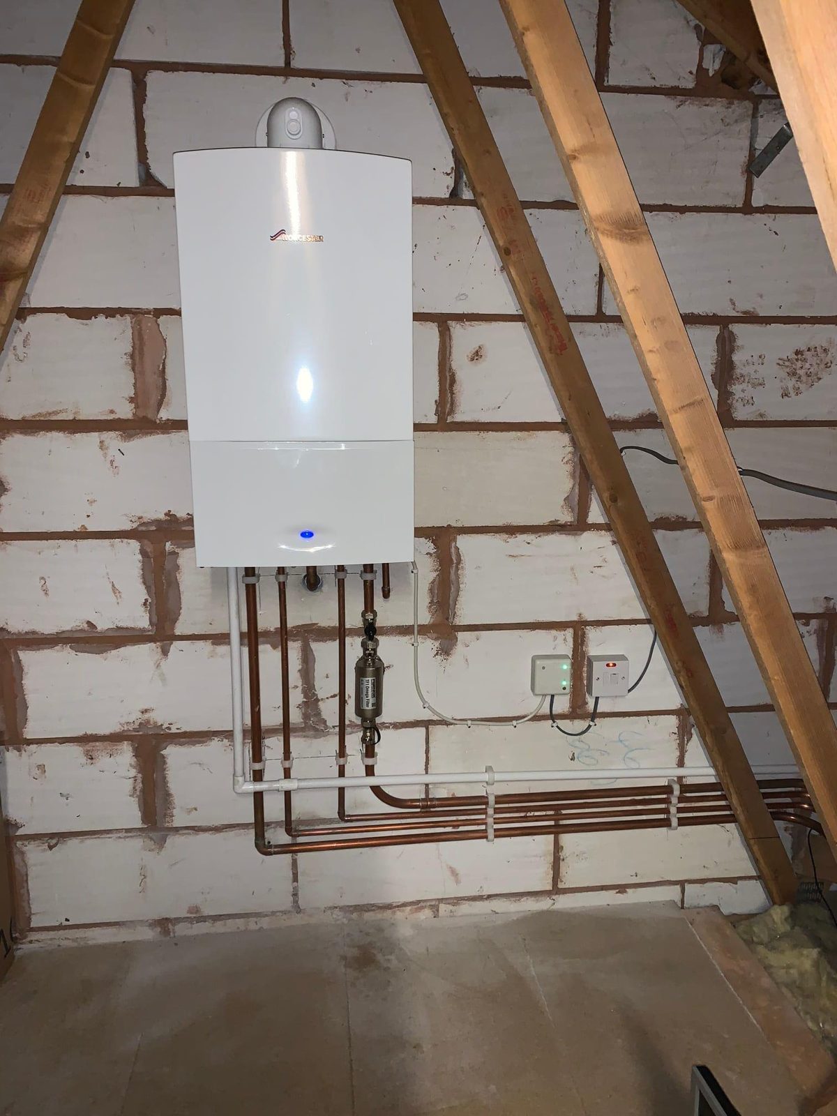 Boiler fitted in a loft on a block wall, pipework run along the wall