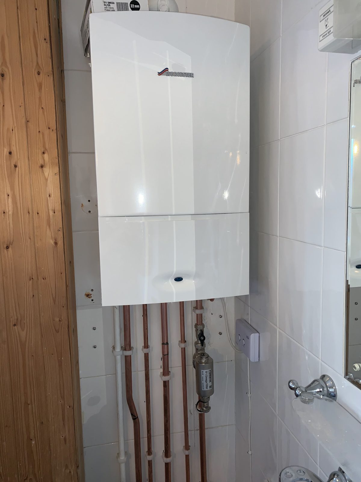 White boiler beside timber cladding, copper pipes running down the wall