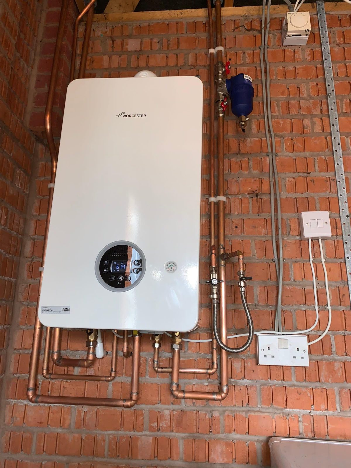 White boiler with a round display fitted on a brick wall, new copper pipework below