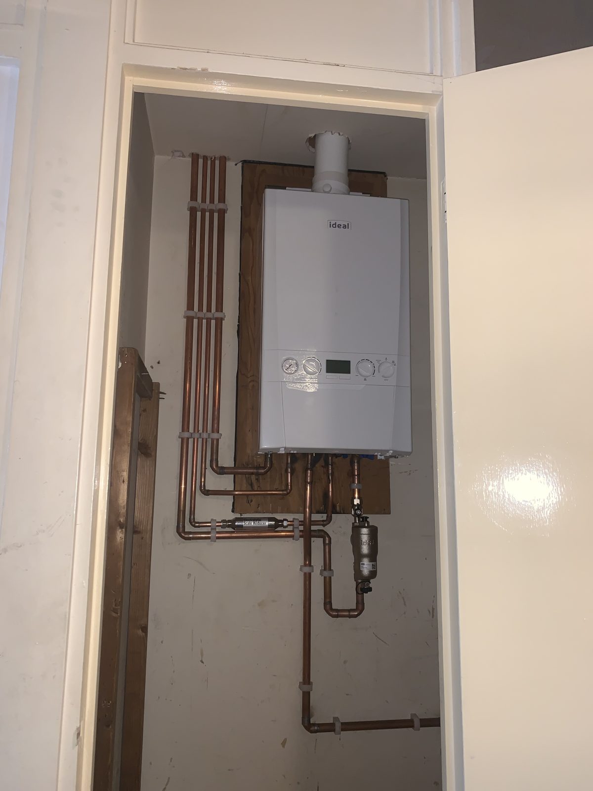 Boiler fitted inside a cupboard with the door open, neat pipework below