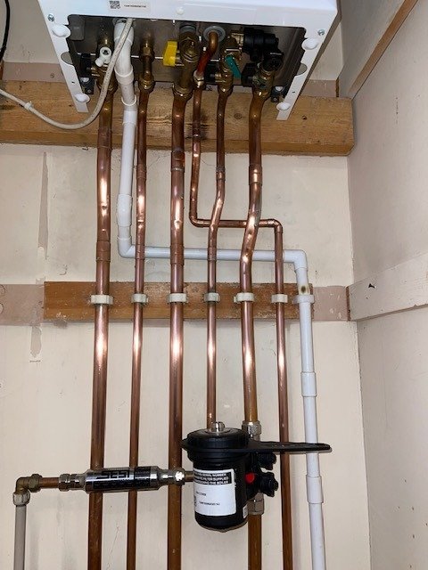 Close-up of copper pipes under a boiler with a magnetic filter fitted