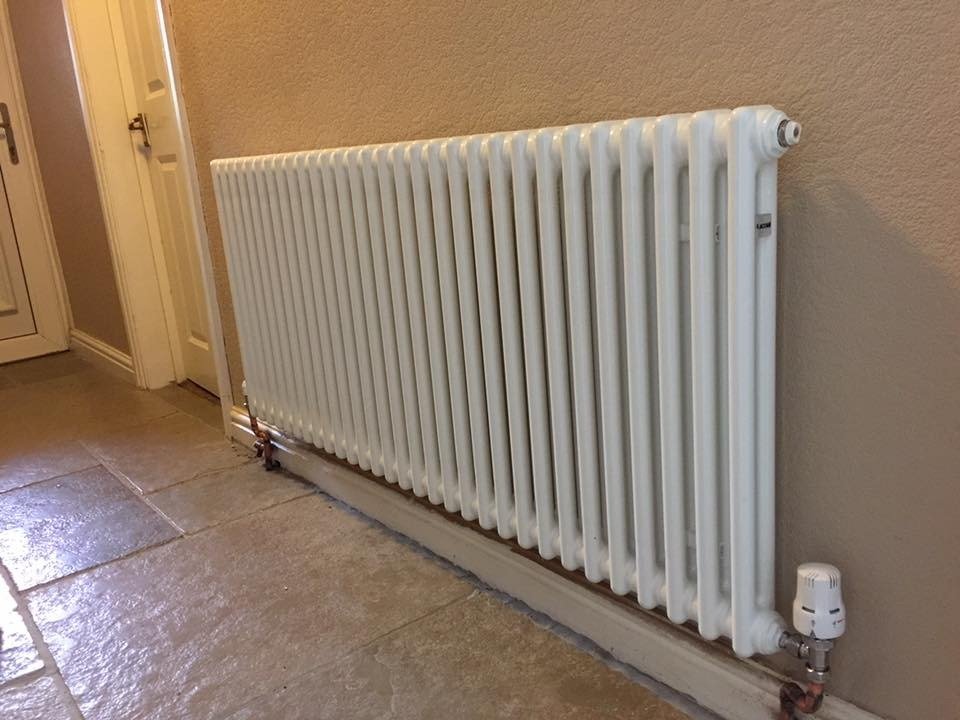 White horizontal column radiator fitted on a stone floor, with a thermostatic valve