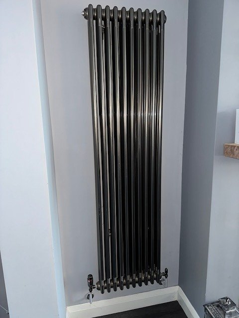 Tall vertical column radiator fitted on a pale wall